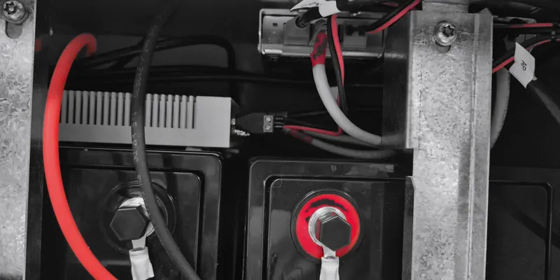 Battery terminals and cabling inside a pole equipment cabinet, one terminal capped in red.