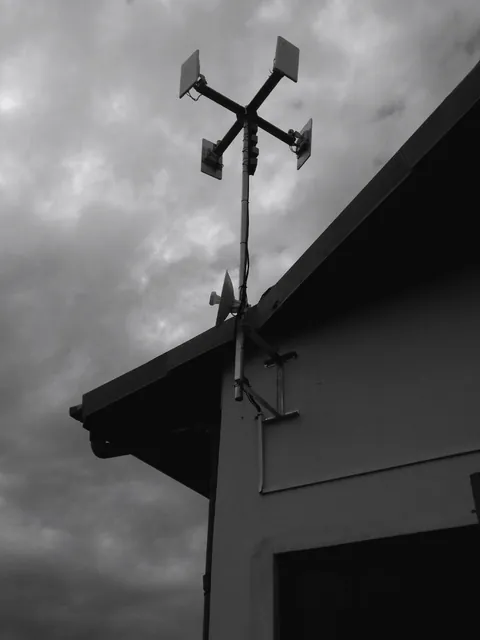 A mast on a building gable carrying four sector access points and a point-to-point link, under storm clouds.